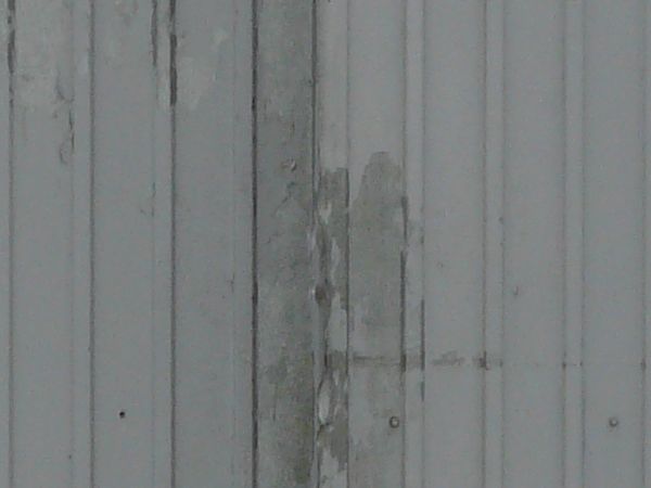 Worn grey metal doors with lined texture on surface and peeling paint.